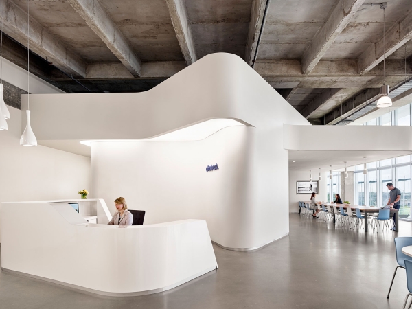 People working inside of a mostly white office building with curved walls and a curved front desk area.